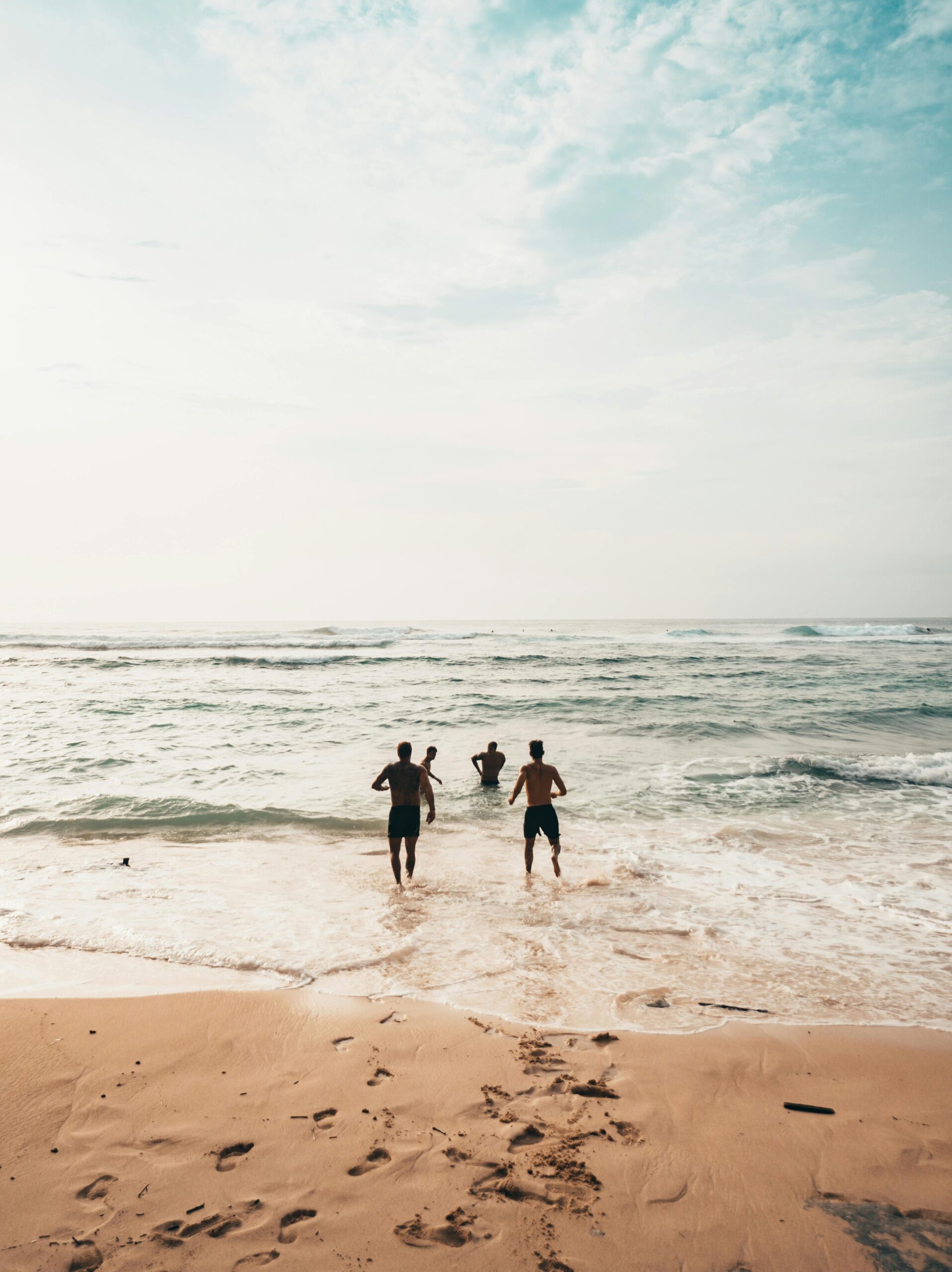 Three friends run into the ocean on a sunny day at a scenic beach in Bali.